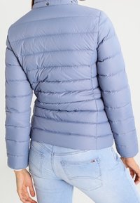 Ljusblå, fodrad pufferjacka med horisontell sömnad, hög krage och tryckknappar, i kombination med ljusa jeans.