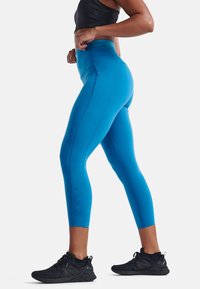 Blå atletiska leggings med hög midja, tillverkade av elastiskt material. Har sömnadsdetaljer och präglat varumärke längs benet.