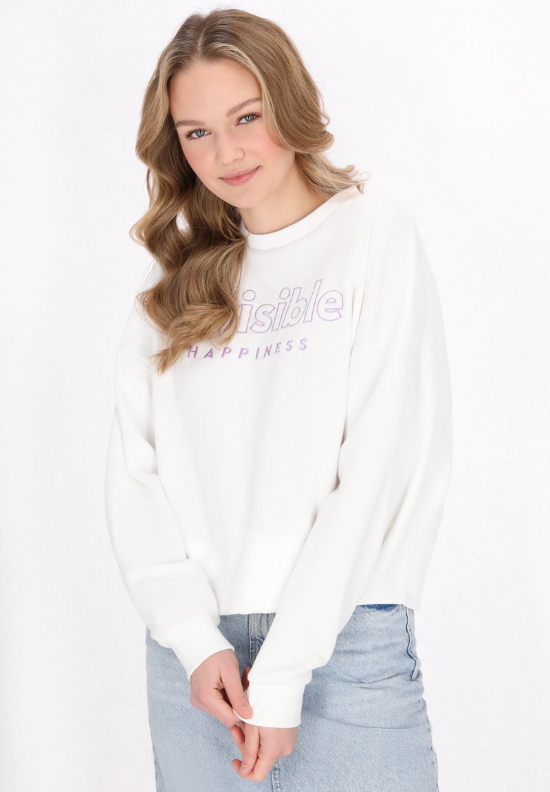 Felpa bianca con spalle scese, testo viola "Invisible" e "Happiness", tessuto morbido, design cropped, abbinata a una gonna di jeans.