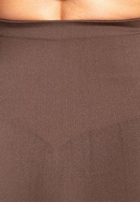 Tissu côtelé marron avec une texture lisse. L'ourlet présente un léger motif en forme de V. Le matériau semble élastique et moulant.