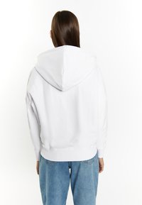 Vit kort hoodie med stor huva, gjord av mjukt material. Ribbat avslut och ärmar, kombinerat med lösa blå jeans. Enkel och minimalistisk design.