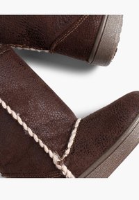 Botas de tobillo marrones hechas de ante texturizado, con acentos trenzados y una suela de goma con un acabado estampado.