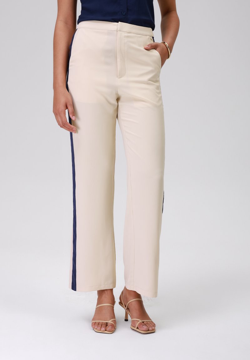 Beige broek met een rechte snit, voorzien van marineblauwe zijkanten. Glad textuur en een hoge tailleontwerp. Zakjes aan beide zijden.