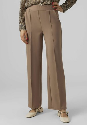 Beige wijde broek van een gladde stof, voorzien van zijzakken en centrale plooien, gecombineerd met crèmekleurige vierkante schoenen.