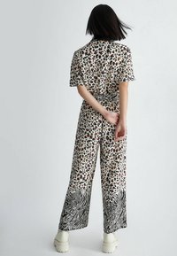 Leopard-print jumpsuit with short sleeves and wide legs, featuring a black and white zebra pattern at the hem. Material appears smooth and lightweight.