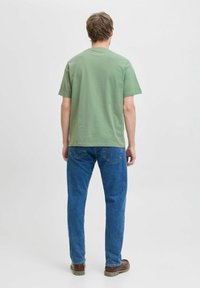 Žalios medvilnės marškinėliai su apvalia iškirpte, trumpomis rankovėmis, derinami su mėlynomis džinsinėmis kelnėmis ir rudais batais. Paprastas dizainas, laisvas pas fitas.