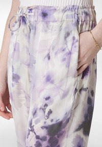 Lätt, pastell-lila blommiga byxor med elastisk midja och dragsko. Har flödande tyg och sidofickor.