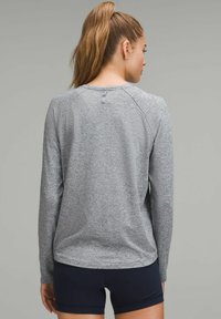 Harmaa pitkähihaista paitaa, jossa on teksturoitu urheilukangas. Ominaisuuksiin kuuluu pyöreä kaulus ja ribbikuvioidut hihansuut. Selässä on pieni ripustuslenkkiyksityiskohta.