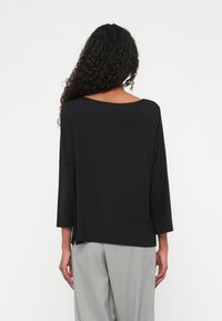 Zwarte lange mouw top met een losse fit en een ronde hals. De stof lijkt zacht en lichtgewicht. Gemaakt met lichte grijze streepjesbroek.