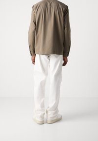 Košile na knoflíky barvy světle hnědé, bílé kalhoty rovného střihu a béžové tenisky. Hladká látka, volný střih, s jednoduchým designem a neutrálními barvami.