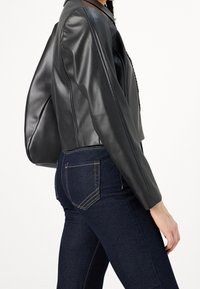 Svart läderjacka i kort modell med en jämn yta och väldefinierade axlar, kombinerad med mörka denimjeans som har subtila sömnadsdetaljer.