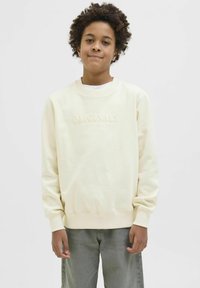 Ljust krämfärgad sweatshirt med texturerad "ORIGINALS"-logotyp. Har en rund halsringning, lång ärm och ribbade manschetter, i kombination med grå byxor.