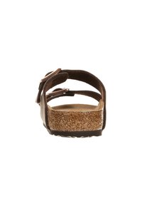 Brun sandal med en korkfotbädd, texturerad sula, justerbara remmar och en mjuk mockaöverdel med öppen bakdesign.