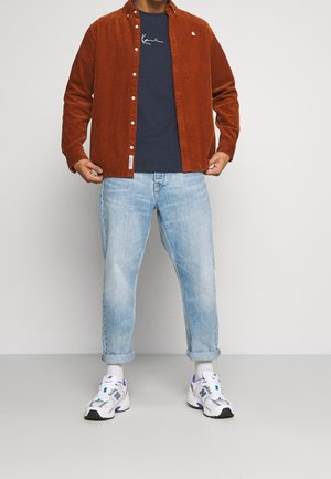 Rustinvärgad kordfløjelskjorte, navy t-shirt, lyseblå opsmøgede jeans og hvide sneakers med lilla detaljer.