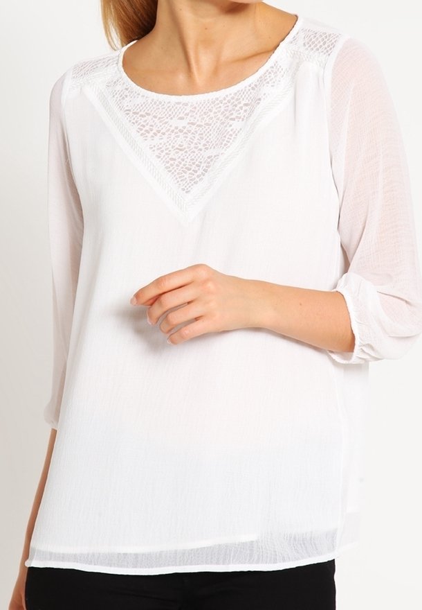 Blusa bianca realizzata in un tessuto leggero e trasparente con un inserto in pizzo sul colletto. Presenta maniche a tre quarti e una vestibilità comoda.
