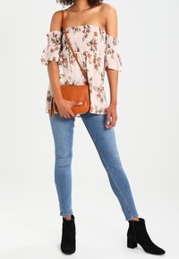 Top rosa chiaro senza spalle con stampa floreale, corpino smock e maniche a sbuffo, abbinato a jeans skinny blu e stivaletti neri alla caviglia.