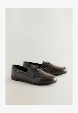 Smeđe kožne čamce s vezicama, srebrnim okovom, zaobljenim vrhom i teksturiranim potplatima. Glatka površina s detaljima šivanja duž bočnih strana.