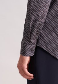 Langarmshirt van donkere stof met een herhalend patroon van kleine, multicoulore cirkels. Voorzien van een knoopmanschet en een afgeronde onderkant.