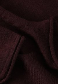 Burgundské pletené látky s jemnou texturou, vystupující s hladkými a žebrovanými oblastmi, uspořádanými v vrstevnatých záhybech.