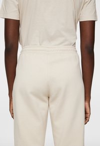 Hellbeige Lounge-Set, bestehend aus einem lässig geschnittenen Shirt und elastischen Hosen. Der Stoff wirkt weich und hat eine glatte Textur.