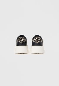 Adidași negri cu tălpi albe, cu un model texturat cu puncte pe spate. Exterior din piele netedă și design cu toc cu amortizare.