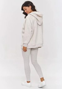 Jasnoszara, oversize'owa bluza z kapturem, w komplecie z dopasowanymi legginsami. Białe sneakersy dopełniają całość. Miękka, gładka struktura materiału.