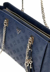 Sac à main en cuir bleu marine avec des motifs floraux embossés, des anses en chaîne argentée et des accessoires en métal. Ouverture zippée en haut, design structuré.