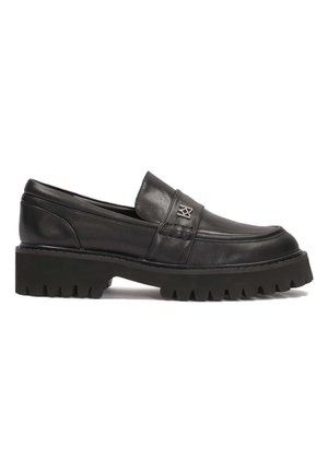 Melna ādas slip-on kurpe ar zemu, masīvu zoli. Tai ir dekoratīva dūriena apdare un logo uz virsmas. Riepu gumijas ārējā zole.