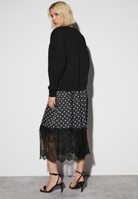 Black oversized sweatshirt paired with a knee-length polka dot skirt, featuring a black lace trim, and black strappy heels.