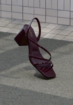 Sandalo bordeaux con tacco alto lucido in vernice, caratterizzato da molteplici sottili cinturini e design con punta quadrata. Tacco spesso e quadrato.