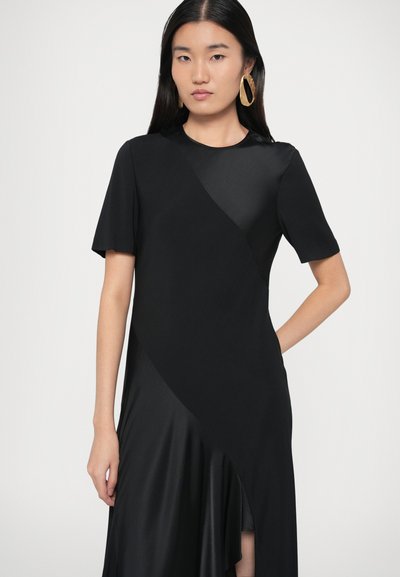 Fekete ruha rövid ujjakkal, ívelt szegéllyel és redős részlettel, valamint matt és szatén textúrák keverékével. Arany kör alakú fülbevalók.