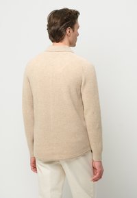 Beige ribbed knit pullover with a collar, long sleeves, and a slightly curved hem. Soft texture with a simple, minimal design.
