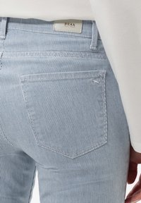 Světle modré pruhované džíny se přiléhavým střihem, s jednou zadní kapsou a značkovou etiketou na pase. Jemná textilie.