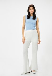 Blauwe getailleerde mouwloze top en witte gemarmerde flared broeken. De outfit heeft verticale patronen en een gladde, zachte textuur. Witte schoenen maken de look compleet.