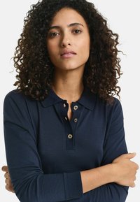 Navy long-sleeve polo shirt featuring a collar, three-button placket, and ribbed cuffs. Made from a smooth texture fabric.