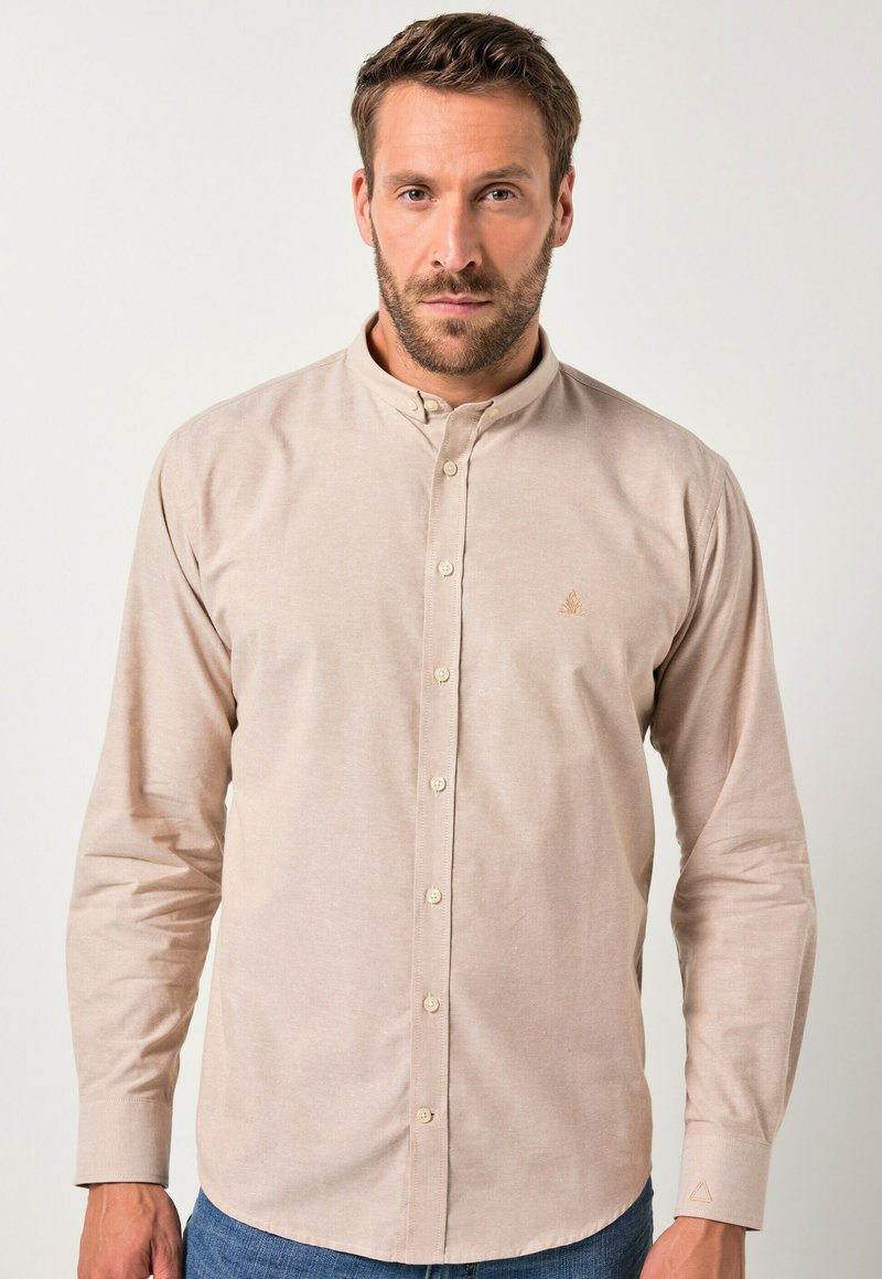 Jasnobeżowa koszula zapinana na guziki z kołnierzem typu stójka, długimi rękawami i subtelnym trójkątnym logo. Miękki bawełniany materiał o gładkiej fakturze.