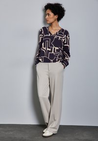 Maglietta a maniche lunghe con scollo a V, patterned blu navy e beige, abbinata a pantaloni beige a gamba larga e sneakers beige. Tessuto morbido.
