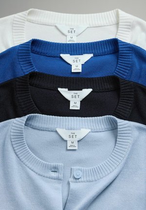 Patru pulovere cu guler rotund prezentate în straturi: alb, albastru, bleumarin și albastru deschis, cu guler nervurat și detalii cu nasturi pe cel albastru deschis.