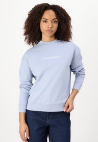 Sweatshirt azul claro com punhos e barra em ribana, com um logo branco "Calvin Klein" centrado no peito; textura lisa.