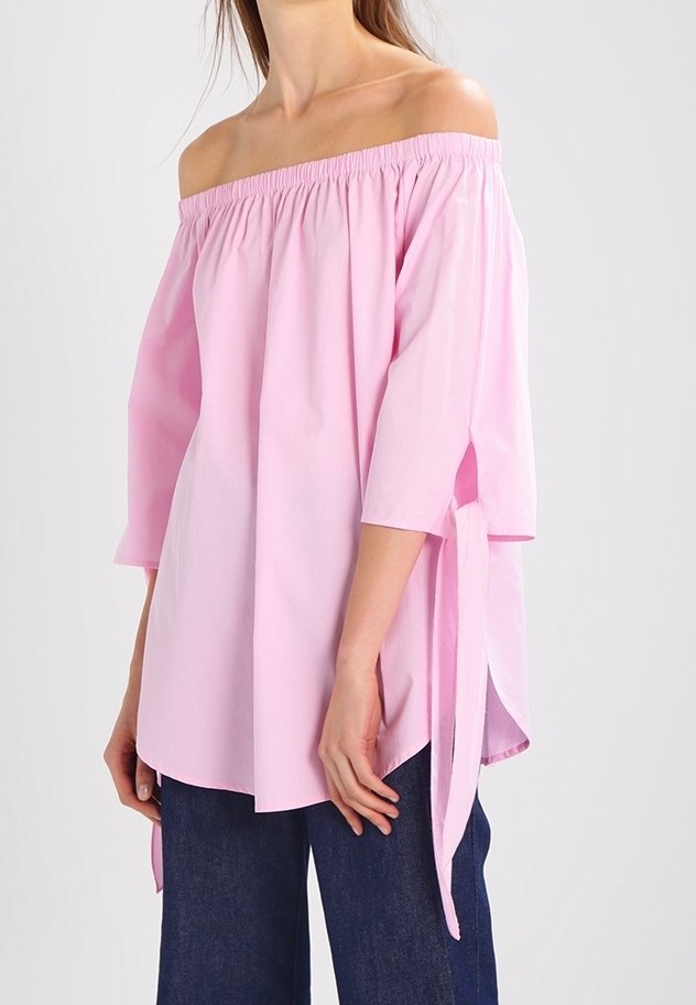 Blusa rosa a spalle scoperte con scollatura elastica, maniche a tre quarti e legacci laterali. Realizzata in tessuto leggero, di consistenza morbida.