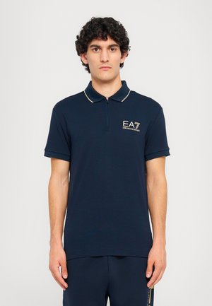 Polo navy blue realizzato in tessuto morbido, con una zip corta, rifiniture in oro a contrasto e il logo EA7 sul lato sinistro del petto.