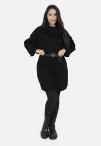 Sort strikket oversized sweaterkjole med en cowl-hals kombineret med et sort bælte med hjerteformet spænde og sorte leggings. Sorte snørestøvler.