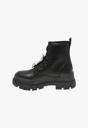 Bottine en cuir noir avec une semelle épaisse et texturée, ornée de lacets décoratifs. Elle présente un bout arrondi et des lacets noirs contrastants.