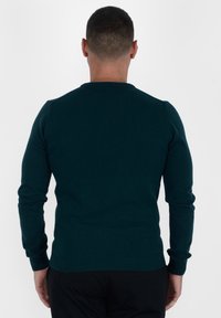 Maglione a maniche lunghe di un blu scuro con scollatura rotonda e polsini e orlo a costine, texture liscia e design aderente.
