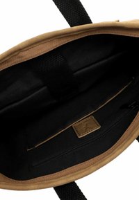 Interno di una borsa in tela color beige con fodera in tessuto nero. Dispone di una tasca con zip e un'etichetta in pelle. Presenta manici testurizzati e rifiniture a spina di pesce.