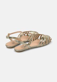 Sandales métalliques dorées avec plusieurs brides croisées et un design à talon ouvert. Elles disposent d'une semelle lisse et d'une petite fermeture à boucle.
