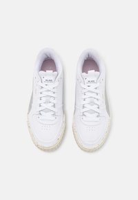 Paire de baskets blanches Puma RE.GEN avec lacets, accents latéraux gris et semelles beiges tachetées sur fond blanc.