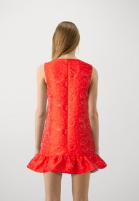 Κόκκινο φόρεμα με δαντέλα με φαρδύ στρίφωμα, λουλούδια, χωρίς μανίκια και υφασμάτινη υφή. Η πλάτη έχει κεντρική ραφή για εφαρμοστό look.