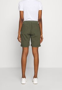 Pantalones cortos hasta la rodilla de color verde oliva con dobladillo enrollado, cintura elástica y textura suave de algodón. Combinados con una camiseta blanca y zapatillas blancas.