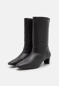 Botas de cuero negro hasta el tobillo con punta afilada, tacón de bloque de altura media y textura suave, que presentan un diseño ajustado y costuras sutiles.